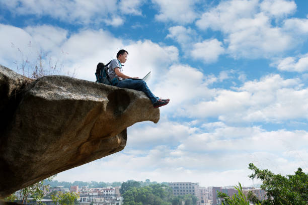 istock Man sitting at the edge of a cliff using laptop 1094751360