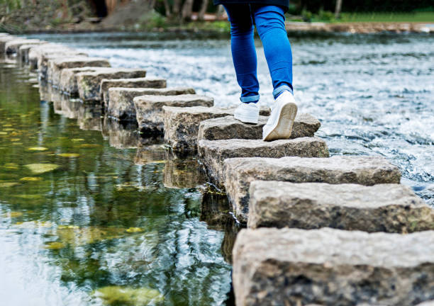 mulher cruzando as pedras de piso em um rio - stepping stone stone stepping footpath - fotografias e filmes do acervo
