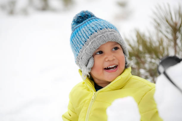 Laughing toddler boy wearing winter clothes in a snow covered mountain. stock photo