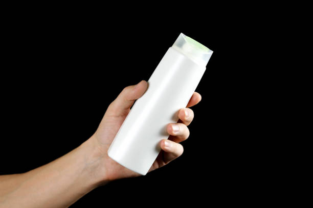 istock Hand holding a white shampoo bottle. Close up. Isolated on black background 1094801002