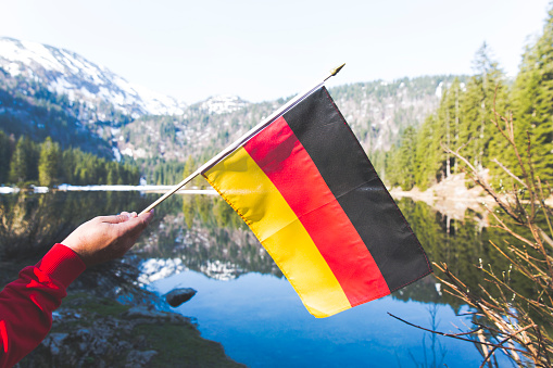 male hiker with red sweater is holding a german flag in the mountains