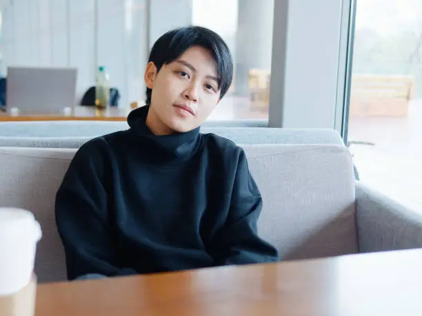 Portrait of cute beautiful young lesbian with short haircut and trendy boyish clothes sitting in coffee shop, friendly Chinese gay girl.