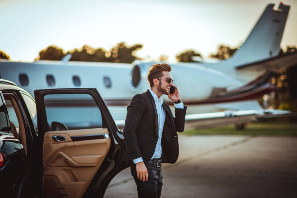 joven empresario rico hablando por un teléfono móvil al salir de un coche de lujo aparcado junto a un avión privado en una pista - millonario fotografías e imágenes de stock