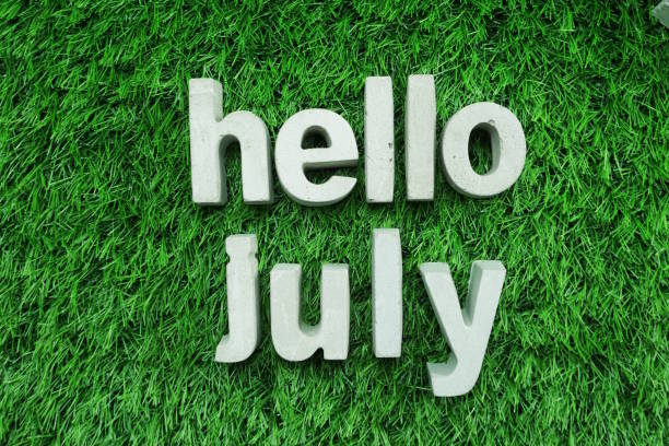 istock Hello July made from concrete alphabet top view on green grass 1094841182