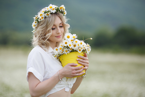 Beautiful girl outdoors with a bouquet of flowers in a field of white daisies,enjoying nature. Beautiful Model with long hair in white dress having fun on summer Field with blooming flowers,Sun Light. Young Happy Woman on spring meadow, countryside