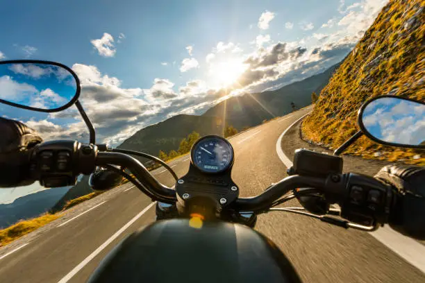 Photo of Motorcycle driver riding in Alpine highway, handlebars view, Austria, Europe.