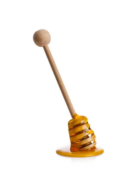 Close up view of a wooden honey dipper standing tilted on white background with honey dripping on the table. Predominant colors are yellow, brown and white. High key DSRL studio photo taken with Canon EOS 5D Mk II and Canon EF 70-200mm f/2.8L IS II USM Telephoto Zoom Lens