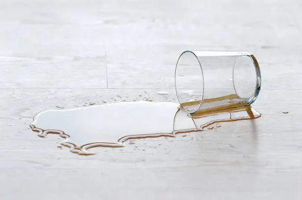water drinking glass falling over the wood laminate flooring with a puddle of water