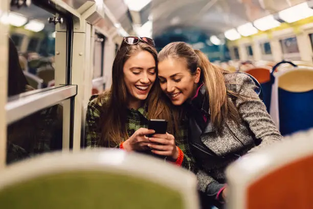 Happy friends traveling at night in public transportation and surfing the net on mobile phone