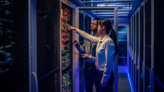 Male and female IT engineers checking servers in server room with help of tablet.