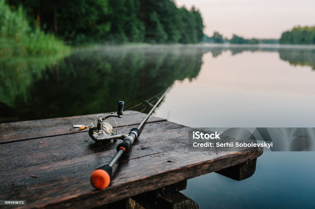 Fishing Rod Spinning Reel On The Background Pier River Bank Sunrise Fog  Against The Backdrop Of Lake Misty Morning Wild Nature The Concept Of Rural  Getaway Article About Fishing Day Stock Photo 