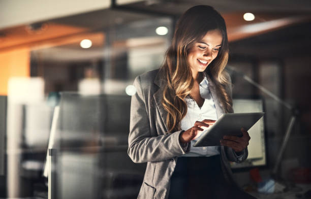 Beat the deadline with technology Cropped shot of a young attractive businesswoman using a tablet while working late at night in the office computer technology people stock pictures, royalty-free photos & images