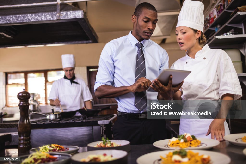 Менеджер-мужчина и женщина-повар с помощью цифрового планшета на кухне - Стоковые фото Отель роялти-фри