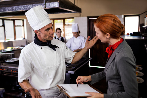 Female manager and male chef interacting with each other in kitchen at hotel