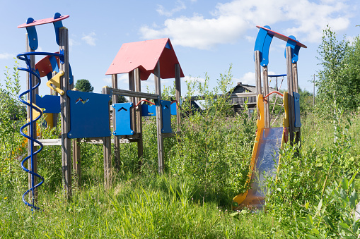 Old neglected playground equipment, overgrown with weeds.