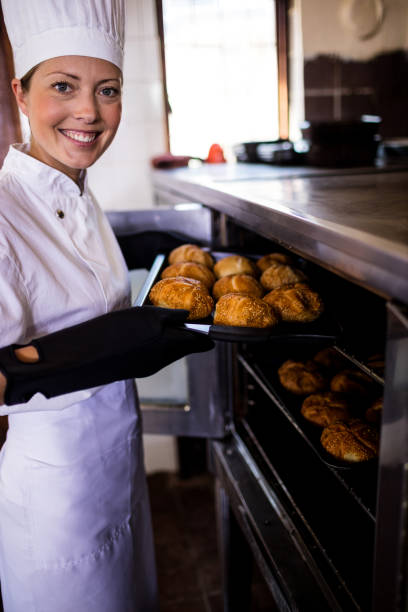 istock Female chefs putting baking tray of kaiser rolls in oven 1094924906