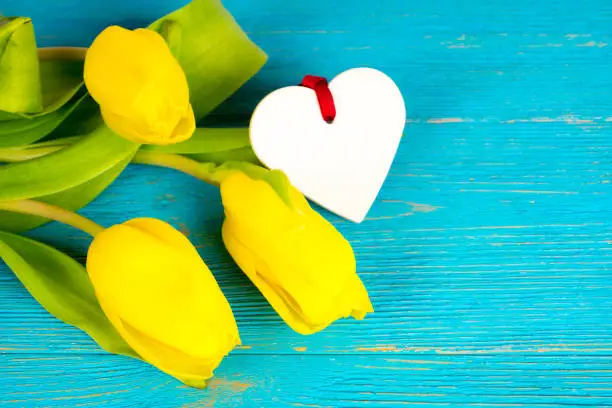 yellow tulips bouquet with heart shape on turquoise rustic wooden background