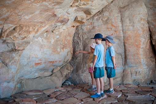 Two young boys and their sister pointing looking at traditional Busman paintings in a cave in the Cederberg South Africa