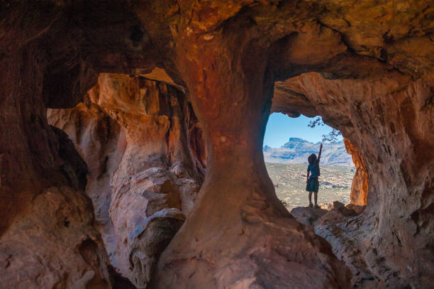 Beautiful Cave Scene with boy reaching high A Young Adventurous Caucasian Boy in a Sandstone cave at Truitjieskraal in the Cederberg reaching to touch a tree branch with an amazing wilderness landscape behind Area South Africa cederberg mountains photos stock pictures, royalty-free photos & images