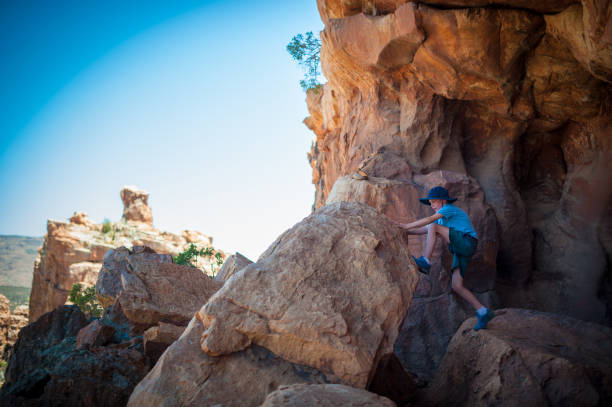 Boy climbing on a rock in a Cave Young Adventurous Caucasian Boy in a Sandstone cave at Truitjieskraal in the Cederberg Wilderness Area South Africa cederberg mountains photos stock pictures, royalty-free photos & images