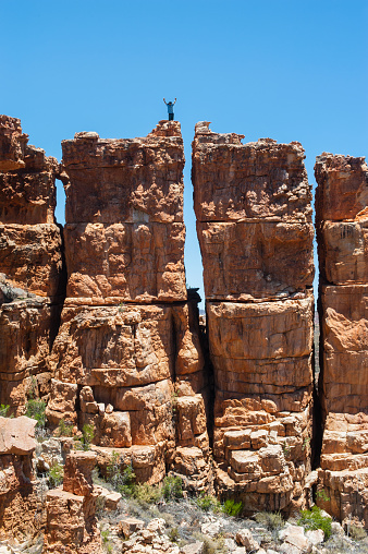 Part of a young Caucasian Boy standing dangerously high up on a distant rock formation ledge with arms raised Truitjieskraal Cederberg South Africa
