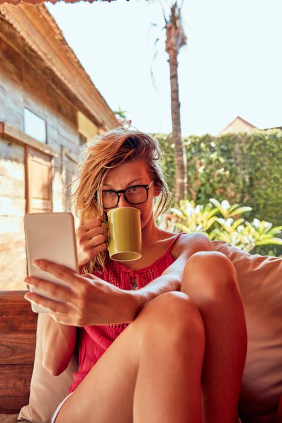 istock Cute woman using smartphone and drinking tea on a porch sofa. 1094942304