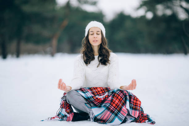 young woman is meditating in the yoga pose on the snow during the winter walk. - winter women zen like photography imagens e fotografias de stock