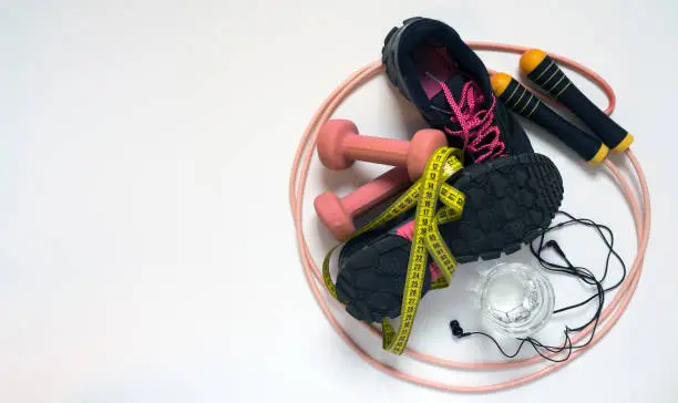 jump rope pink, black sneakers with crimson laces, pink dumbbells and tape measure on a white background, there is a place for an inscription