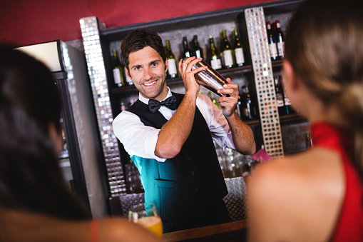 Bartender shaking cocktail in cocktail shaker at bar counter in nightclub