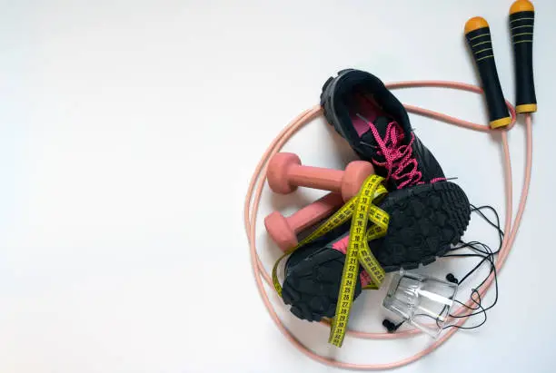 jump rope pink, black sneakers with crimson laces, pink dumbbells and tape measure on a white background, there is a place for an inscription