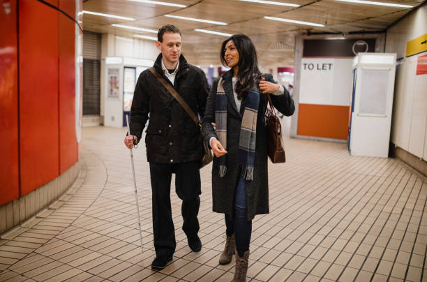 Leaving the Subway Station Together Visually impaired man walking with his friend leaving a subway station, he is using a white walking cane for guidance as well as holding his friends arm. blindness stock pictures, royalty-free photos & images