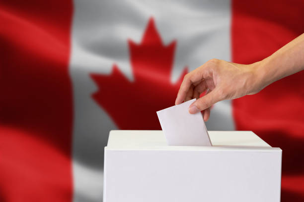 istock Close-up of human hand casting and inserting a vote and choosing and making a decision what he wants in polling box with Canada flag blended in background 1094986630