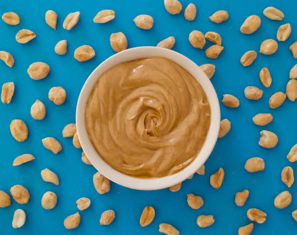 Smooth and creamy peanut butter and peanuts on blue. Top down view.