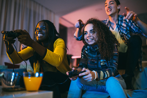 Group of cheerful multi-ethnic people spending good time together while playing video games in living room at night