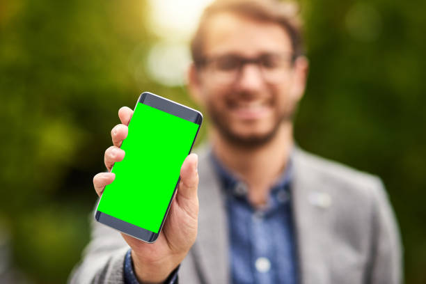 Cropped shot of an unrecognizable businessman holding a mobile phone with a green screen outdoors