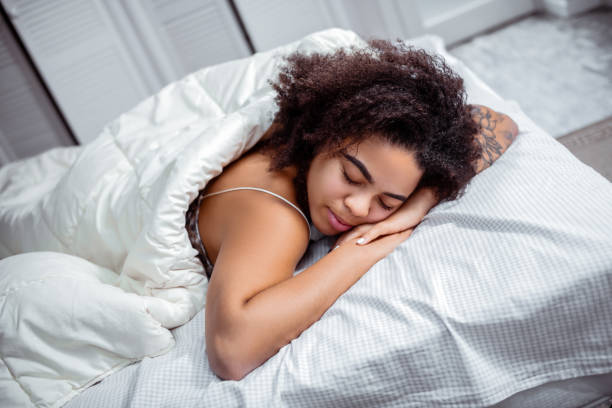 Curly short-haired lady putting head down on connected hands Dark-skinned woman resting. Curly short-haired lady putting head down on connected hands during deep sleep face down stock pictures, royalty-free photos & images