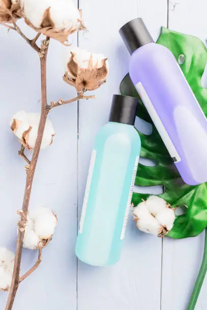 Flat lay cosmetics composition style. Natural cosmetics in bottles. Color liquid in transparent bottles on tropical leaves and cotton and wooden table