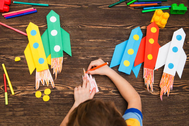 criança pré-escolar em criatividade em casa. criança feliz faz foguetes de papel. criatividade infantil. crianças criativas brincar com artesanato.
ferramentas e materiais para a criatividade de arte infantil na tabela. - toy spaceship inspiration ideas - fotografias e filmes do acervo