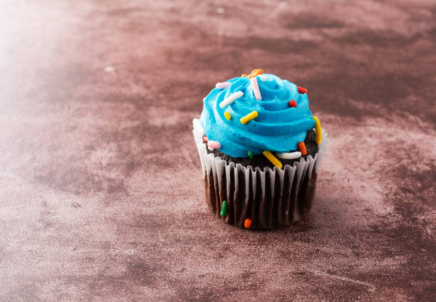 istock A single blue frosted chocolate cupcake on a maroon background. 1095040458