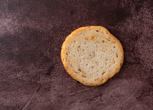 Overhead view of a single sesame round melba toast on a maroon background.