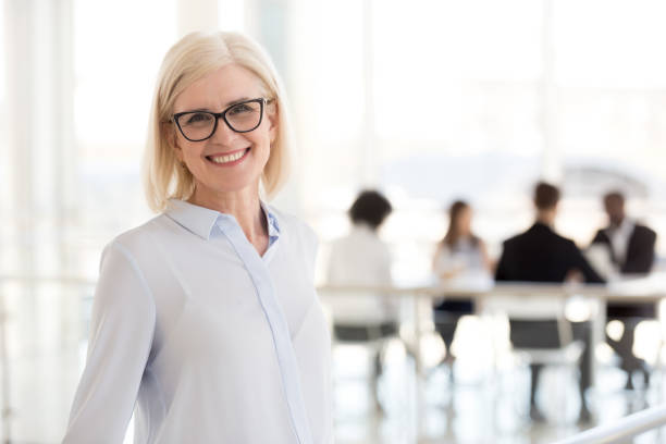 Smiling mature attractive businesswoman in glasses looking in camera Smiling mature attractive businesswoman in glasses looking in camera, happy friendly middle aged female executive, older team leader or business coach mentor posing in office, headshot portrait director stock pictures, royalty-free photos & images