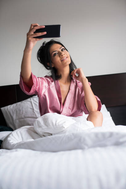 Woman lying down watching cell phone Woman lying on her bed, wearing her pink pajamas, watching her cell phone, playing with him and taking a selfie, in the comfort of her room tecnología inalámbrica stock pictures, royalty-free photos & images