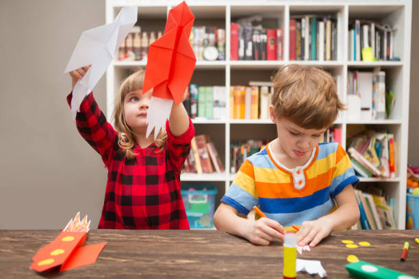 duas crianças prées-escolar em criatividade em casa. crianças faz foguetes de papel e jogar feliz. criatividade infantil. crianças criativas brincar com artesanato. - preschool child craft preschooler - fotografias e filmes do acervo