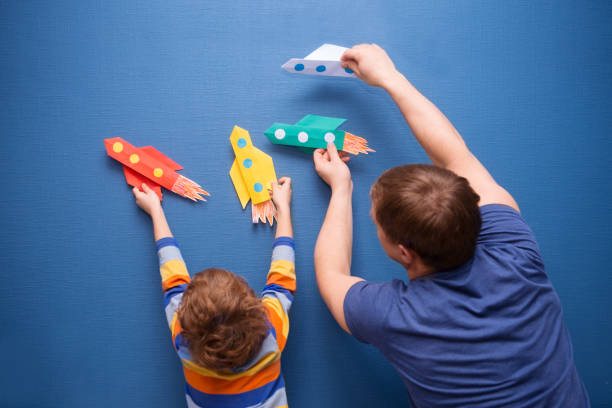 Father and little son are playing with rocket made of paper in the home. Cheerful time together at home. preschool Child in creativity in the home. stock photo
