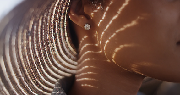 Extreme close up of Black woman with sunhat and diamond earing. Rays of light shining through a hat onto a woman's face