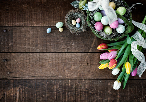 Easter Spring Tulips and a Basket of Easter Eggs on an old Wood Background