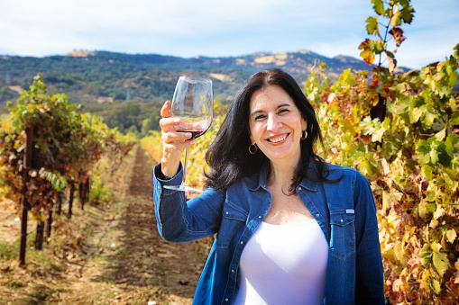 Woman drinking red wine at vineyard. Female farmer holding wineglass and bottle and tasting her homemade wine