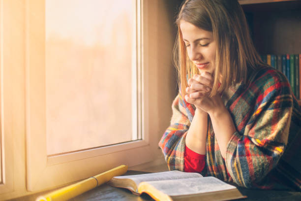 Beautiful woman praying having the Bible opened in front of he stock photo