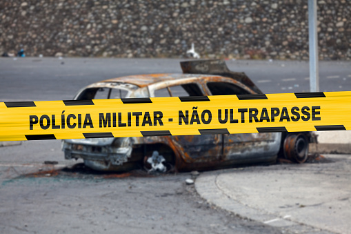 Car burnt by a pyromaniac with a police tape with written in it in Portuguese \
