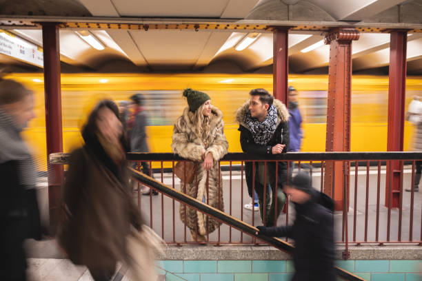 Wide shot of a young couple talking while waiting for their train on a subway station Cheerful couple in love enjoying Berlin at Christams season standing on subway platform stock pictures, royalty-free photos & images
